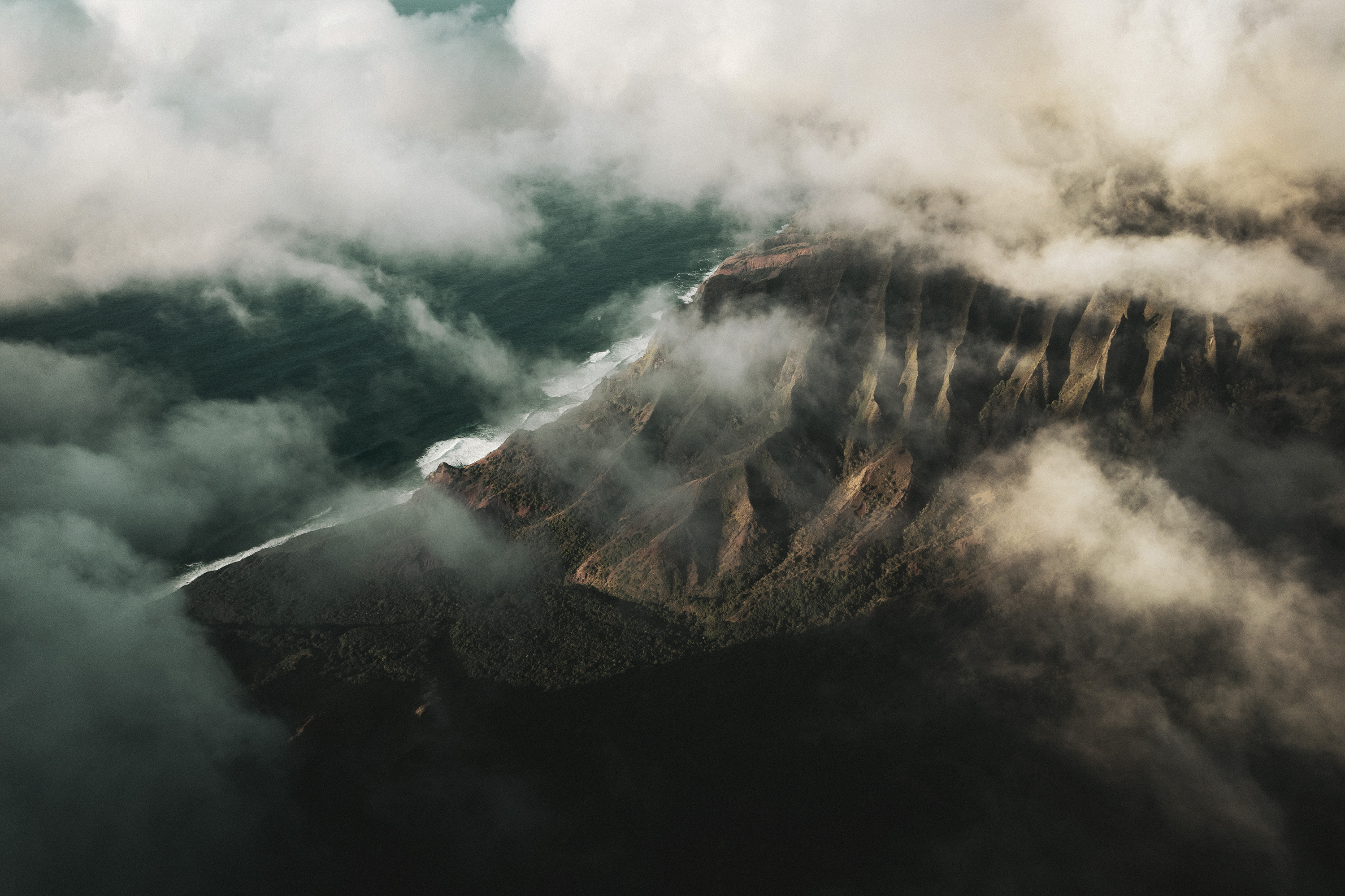 Aerial view of a dramatic coastline with clouds rolling over a mountain ridge meeting the ocean